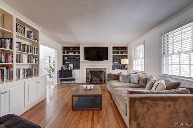 living room featuring ornamental molding, a fireplace, light wood-style floors, and built in shelves