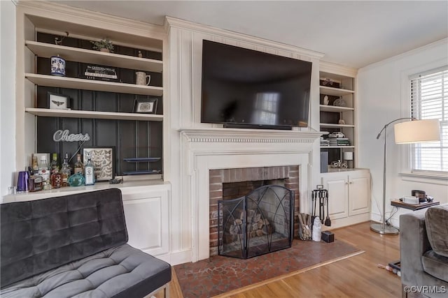 living room featuring ornamental molding, a brick fireplace, wood finished floors, and built in shelves