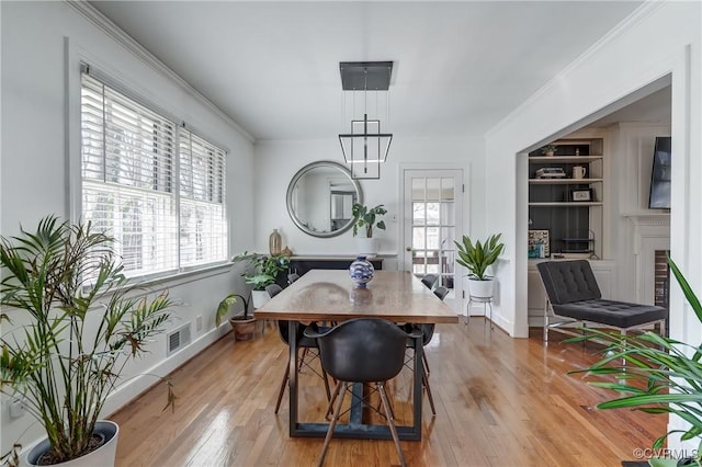 dining room with built in shelves, light wood-style floors, visible vents, and crown molding