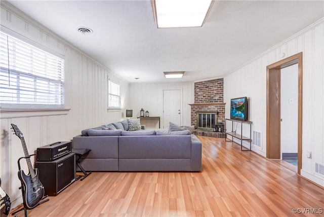 living room with a brick fireplace, visible vents, and light wood-style flooring