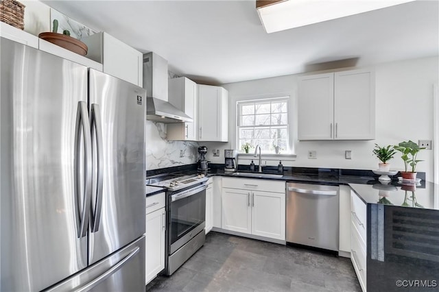 kitchen featuring dark countertops, wall chimney exhaust hood, appliances with stainless steel finishes, and a sink