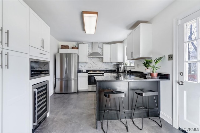 kitchen with wine cooler, stainless steel appliances, a sink, a peninsula, and wall chimney exhaust hood