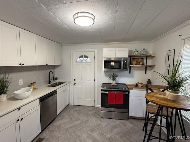 kitchen featuring decorative backsplash, stainless steel appliances, light countertops, white cabinetry, and a sink