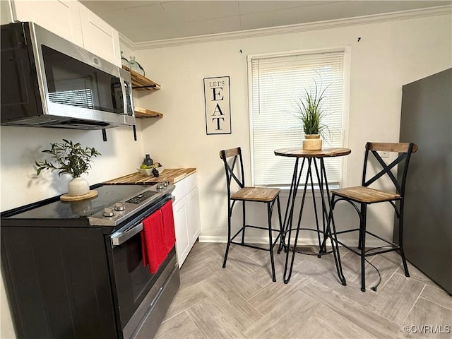 kitchen with electric range, baseboards, stainless steel microwave, crown molding, and white cabinetry