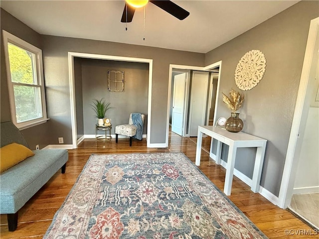 living area with a ceiling fan, baseboards, and wood finished floors