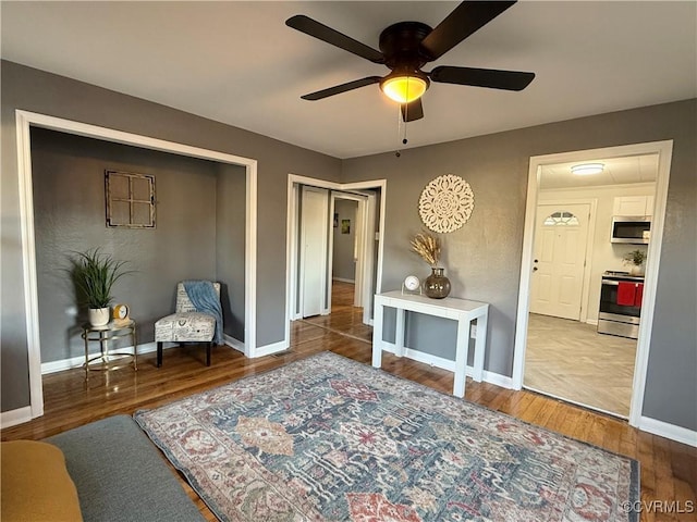 living area featuring a ceiling fan, baseboards, and wood finished floors