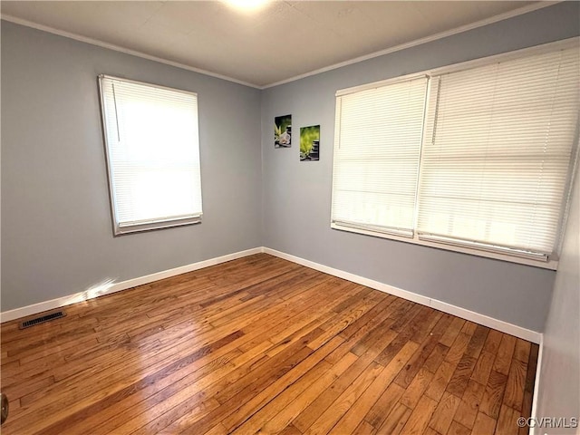 empty room with hardwood / wood-style flooring, baseboards, visible vents, and ornamental molding