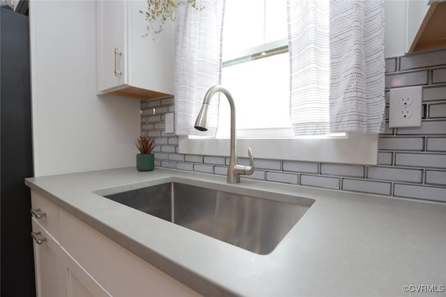 room details featuring light countertops, backsplash, white cabinets, a sink, and fridge