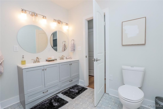 bathroom with baseboards, a sink, toilet, and double vanity