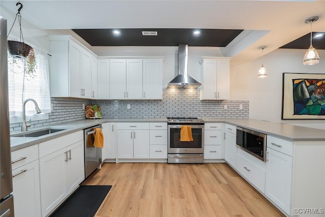 kitchen featuring stainless steel appliances, light countertops, a sink, wall chimney range hood, and a peninsula