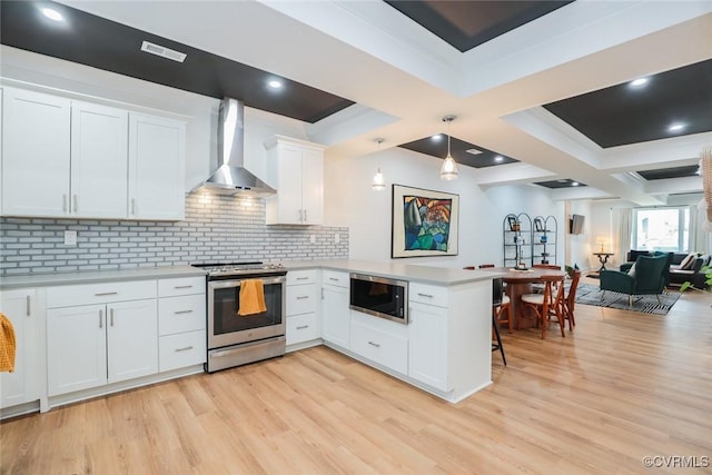 kitchen featuring light wood finished floors, a peninsula, stainless steel appliances, light countertops, and wall chimney range hood