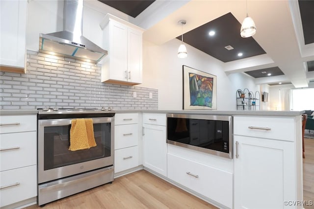 kitchen with light countertops, appliances with stainless steel finishes, light wood-style floors, a peninsula, and wall chimney exhaust hood