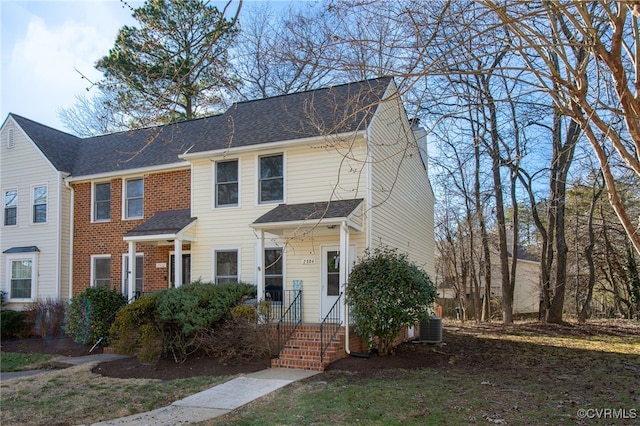 view of front facade featuring a shingled roof, brick siding, a chimney, and central AC unit