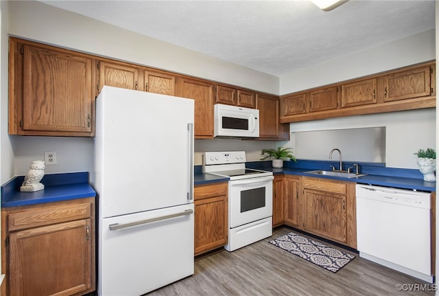 kitchen with white appliances, brown cabinetry, light wood-style flooring, a textured ceiling, and a sink