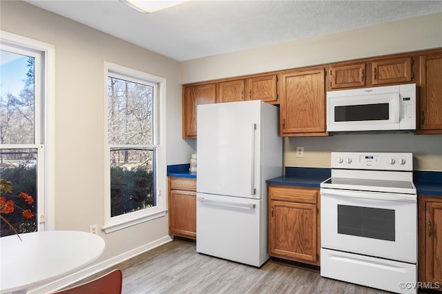 kitchen featuring light wood finished floors, white appliances, brown cabinetry, and dark countertops