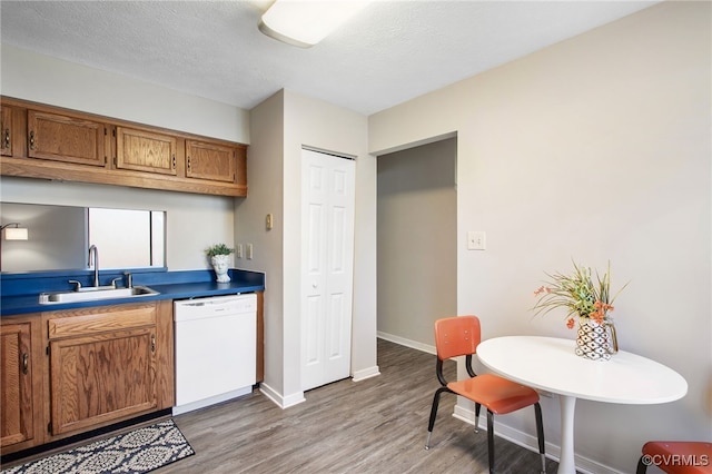 kitchen featuring a textured ceiling, a sink, light wood-type flooring, brown cabinets, and dishwasher