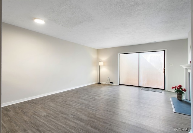 unfurnished living room with a textured ceiling, baseboards, and wood finished floors