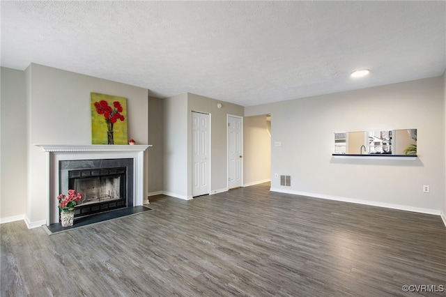 unfurnished living room featuring wood finished floors, a fireplace with flush hearth, visible vents, and baseboards