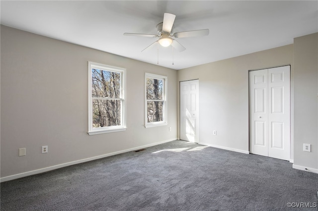 unfurnished bedroom with baseboards, dark carpet, a ceiling fan, and multiple closets