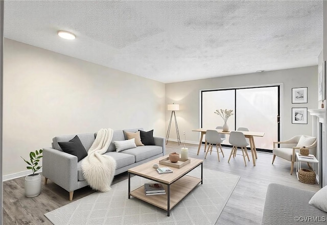 living room with a fireplace, a textured ceiling, baseboards, and wood finished floors