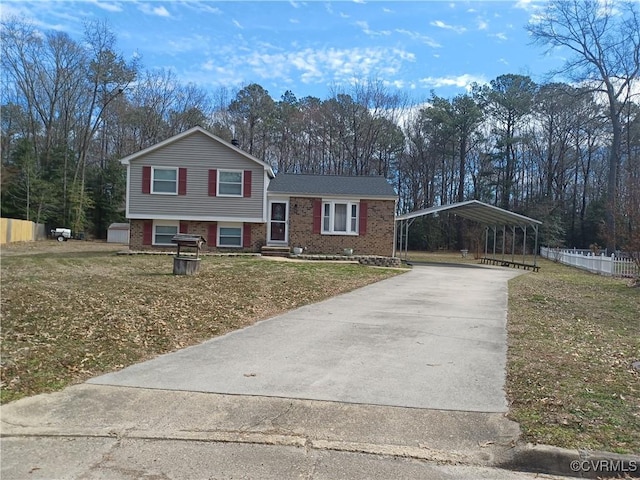 tri-level home with driveway, brick siding, fence, a carport, and a front yard