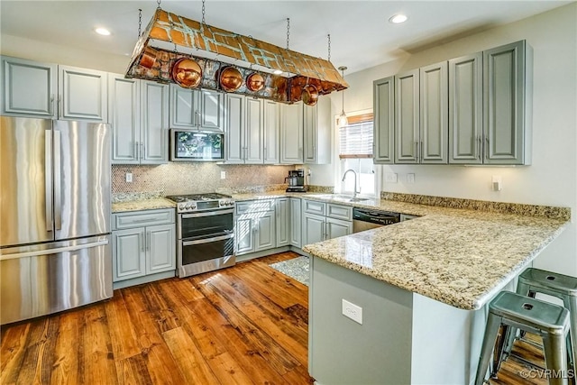 kitchen with light stone counters, stainless steel appliances, a peninsula, a sink, and dark wood finished floors