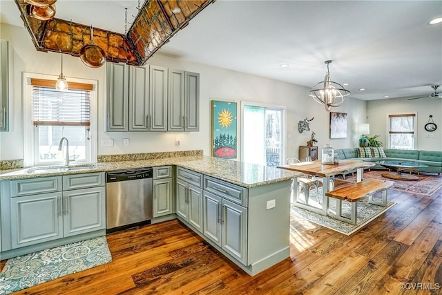 kitchen with dark wood-style floors, a sink, light stone countertops, dishwasher, and a peninsula