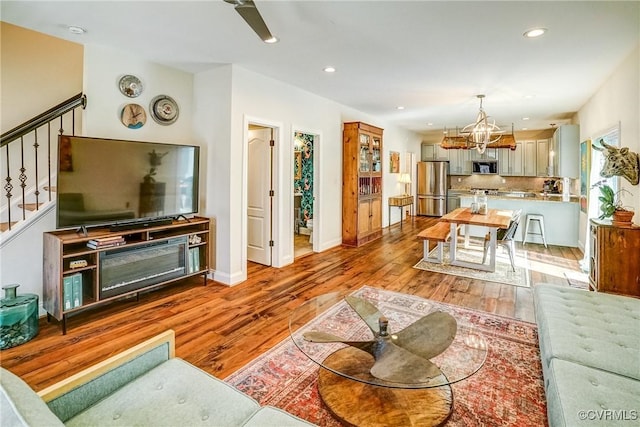 living area with light wood-style floors, recessed lighting, an inviting chandelier, and stairs