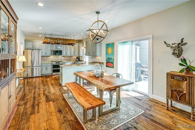 kitchen featuring a notable chandelier, gray cabinetry, appliances with stainless steel finishes, backsplash, and dark wood finished floors