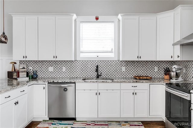 kitchen featuring appliances with stainless steel finishes, white cabinets, a sink, and wall chimney exhaust hood