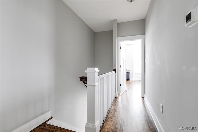 hall with wood finished floors, an upstairs landing, and baseboards