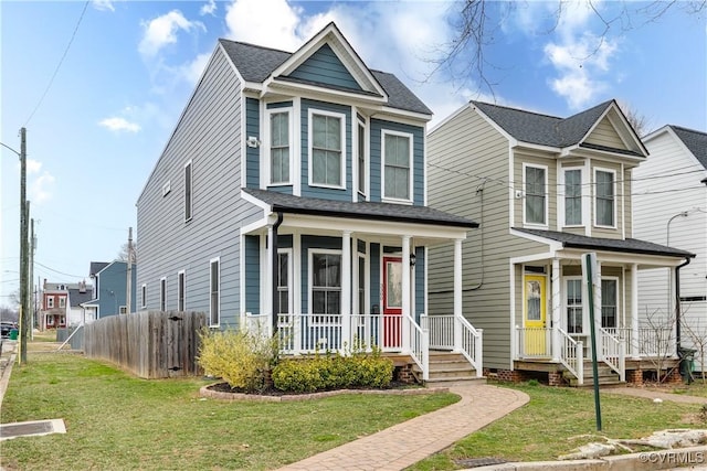 traditional home with a porch, a front yard, fence, and a shingled roof