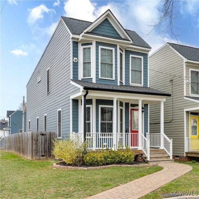 traditional-style house featuring covered porch, a front lawn, a shingled roof, and fence