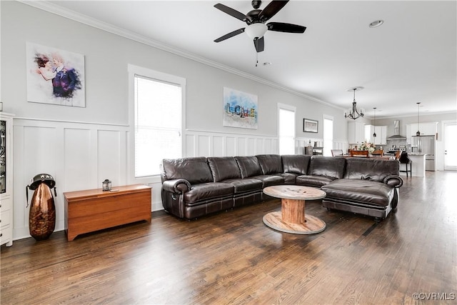 living room featuring a wainscoted wall, dark wood-type flooring, crown molding, and ceiling fan with notable chandelier