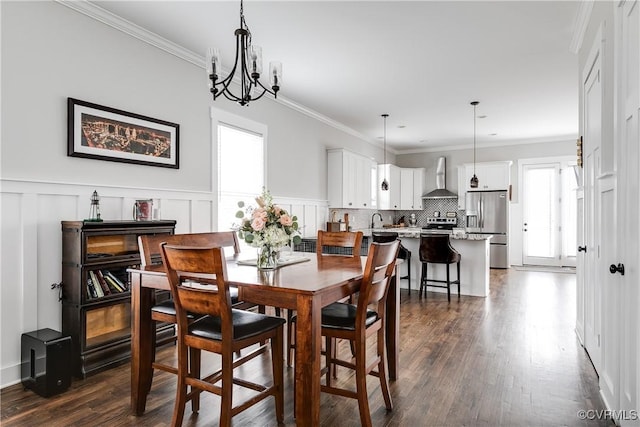 dining room featuring dark wood-style flooring, crown molding, a decorative wall, and an inviting chandelier