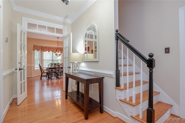 stairs with french doors, ornamental molding, wood finished floors, a chandelier, and baseboards