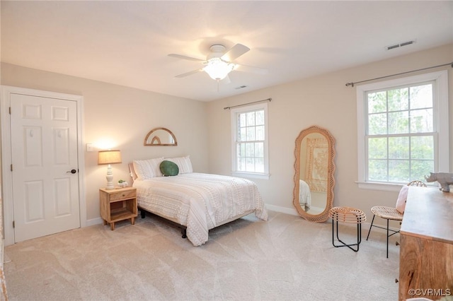 bedroom featuring a ceiling fan, light colored carpet, visible vents, and multiple windows