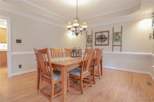 dining area with ornamental molding, light wood finished floors, and a raised ceiling