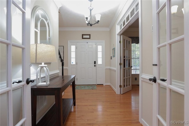 entryway with light wood-type flooring, an inviting chandelier, and ornamental molding