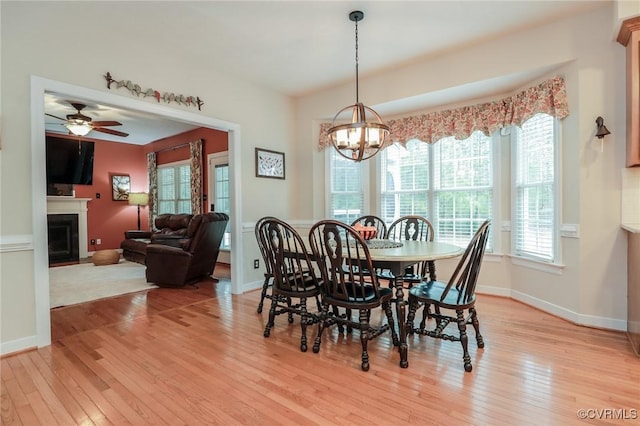 dining space featuring light wood-style floors, a fireplace, baseboards, and ceiling fan with notable chandelier