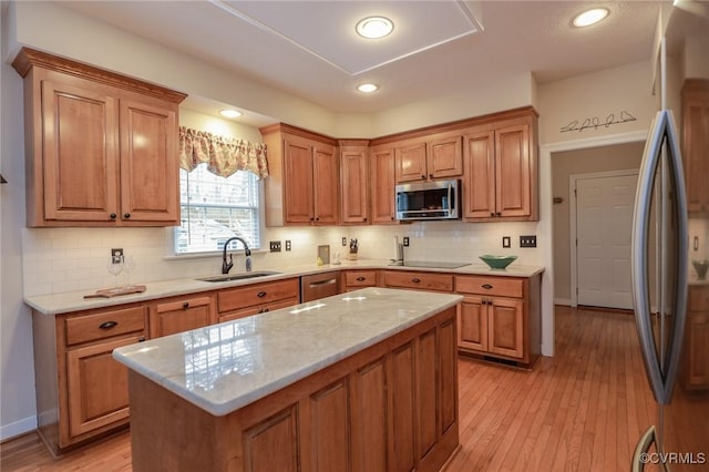 kitchen featuring backsplash, appliances with stainless steel finishes, a sink, a kitchen island, and light wood-type flooring