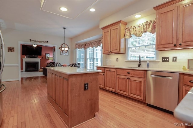 kitchen featuring a center island, a fireplace with raised hearth, light wood-style flooring, stainless steel dishwasher, and a sink