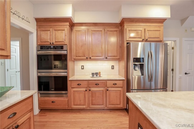 kitchen with light stone countertops, light wood finished floors, appliances with stainless steel finishes, and decorative backsplash