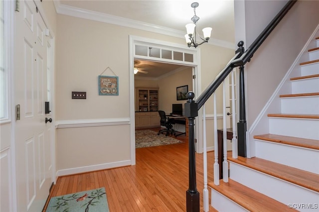 foyer entrance featuring a notable chandelier, light wood-style floors, stairway, and crown molding