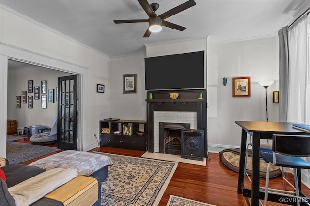 living room with crown molding, a brick fireplace, wood finished floors, and ceiling fan