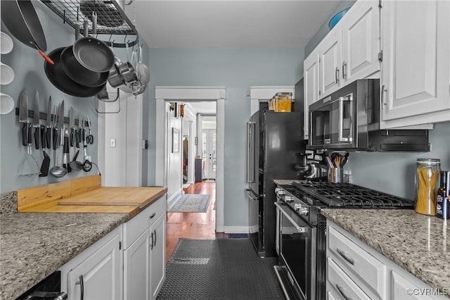 kitchen with stainless steel range with gas stovetop, white cabinetry, freestanding refrigerator, and baseboards