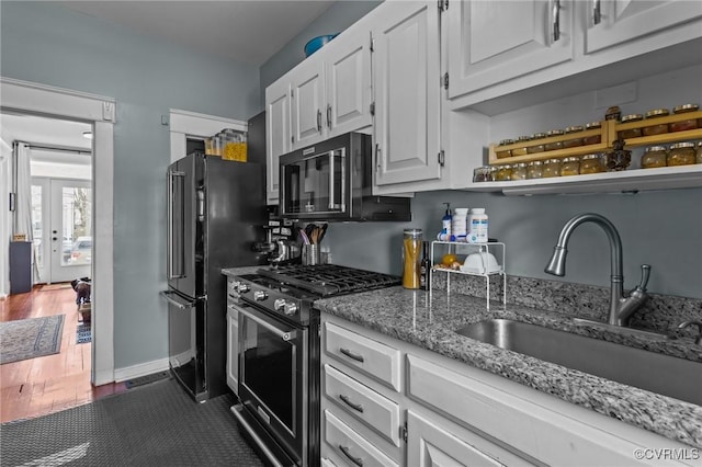 kitchen featuring black appliances, dark wood finished floors, light stone counters, white cabinetry, and a sink