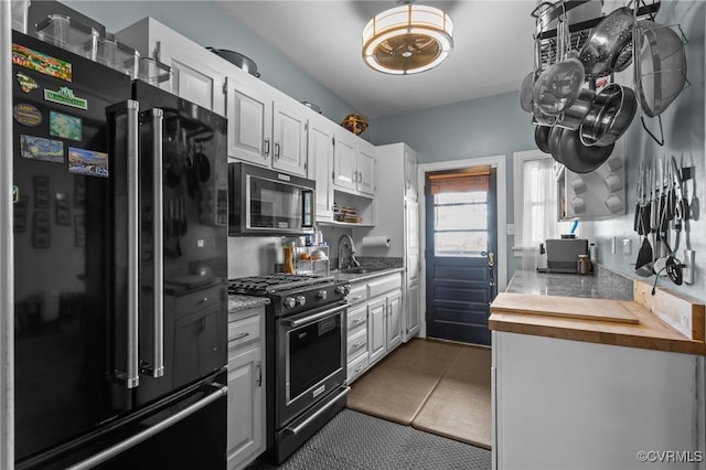 kitchen with butcher block countertops, tile patterned floors, white cabinets, black appliances, and a sink