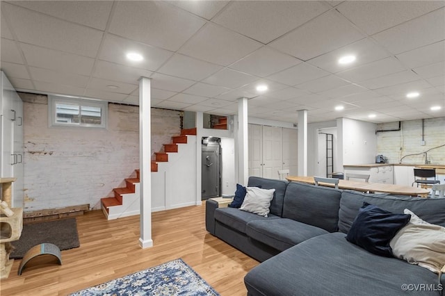 living room with a drop ceiling, recessed lighting, stairs, and light wood-style floors