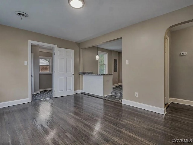 empty room with visible vents, arched walkways, dark wood finished floors, and baseboards